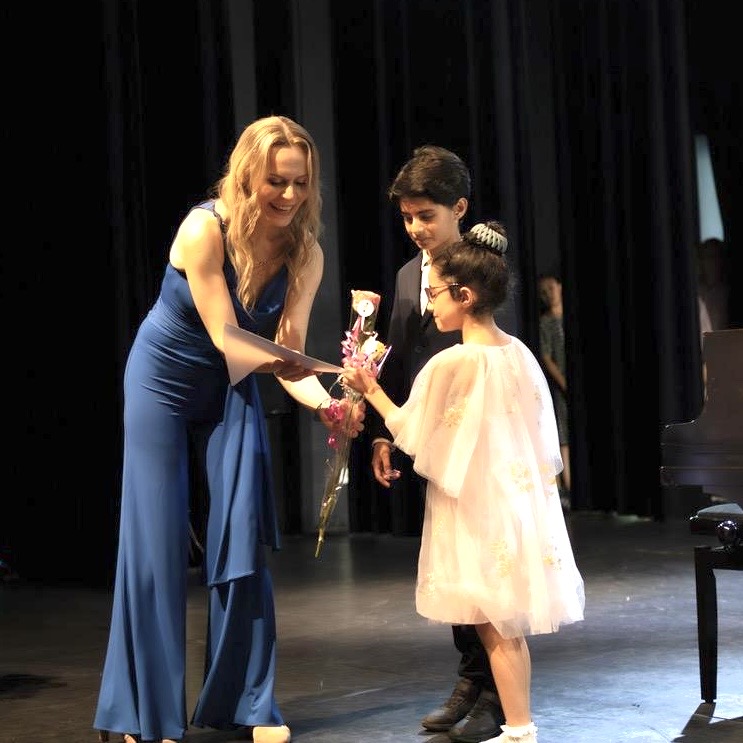 Hülya Keser presenting flowers to a young student on stage